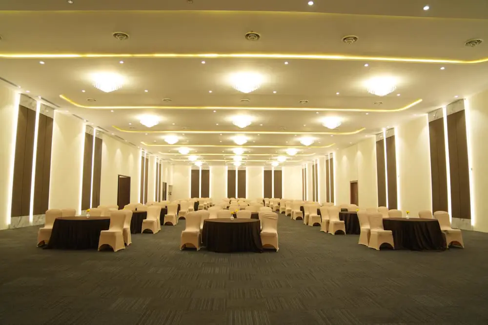 A long carpeted hall with cove lighting, laid with round tables