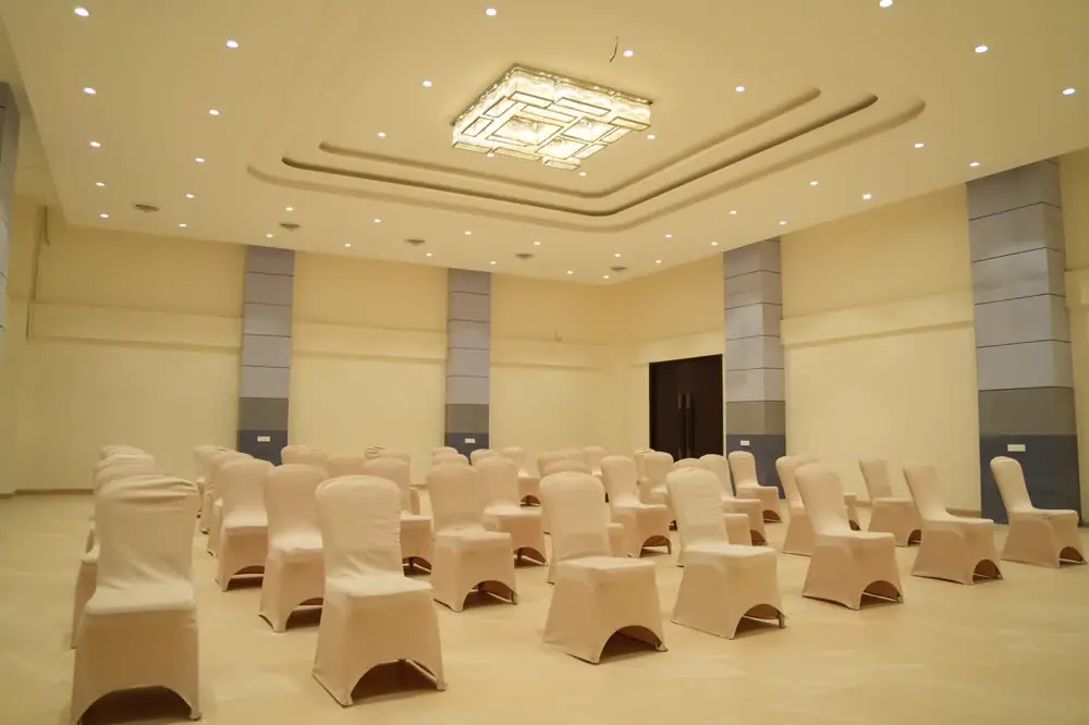 Covered chairs in rows under a chandelier on a marble floor