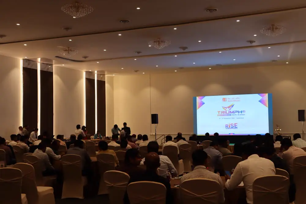 A full conference hall facing a lit stage and screen