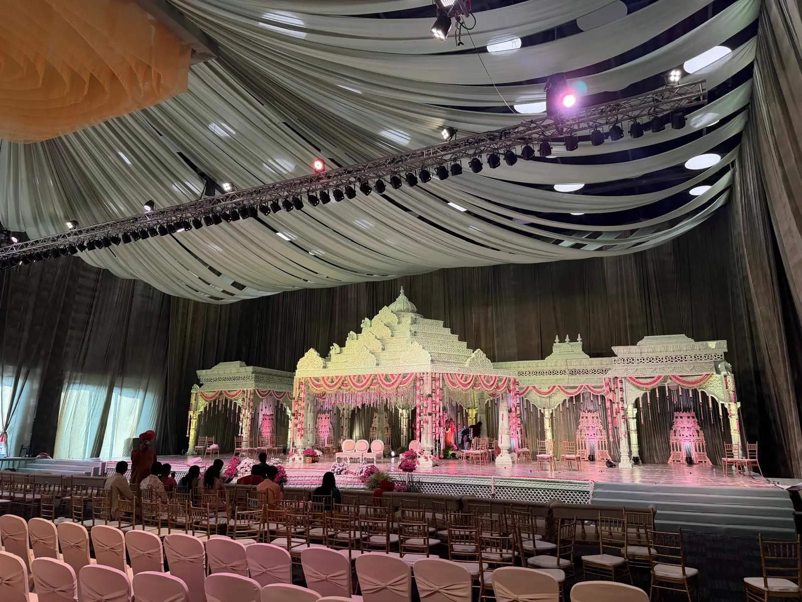 A draped, high-ceilinged wedding hall with a carved mandap