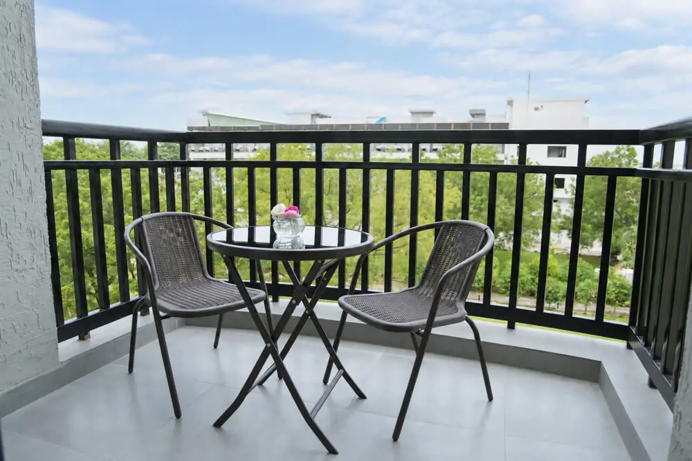 A room balcony with a bistro table and two chairs, trees beyond the railing