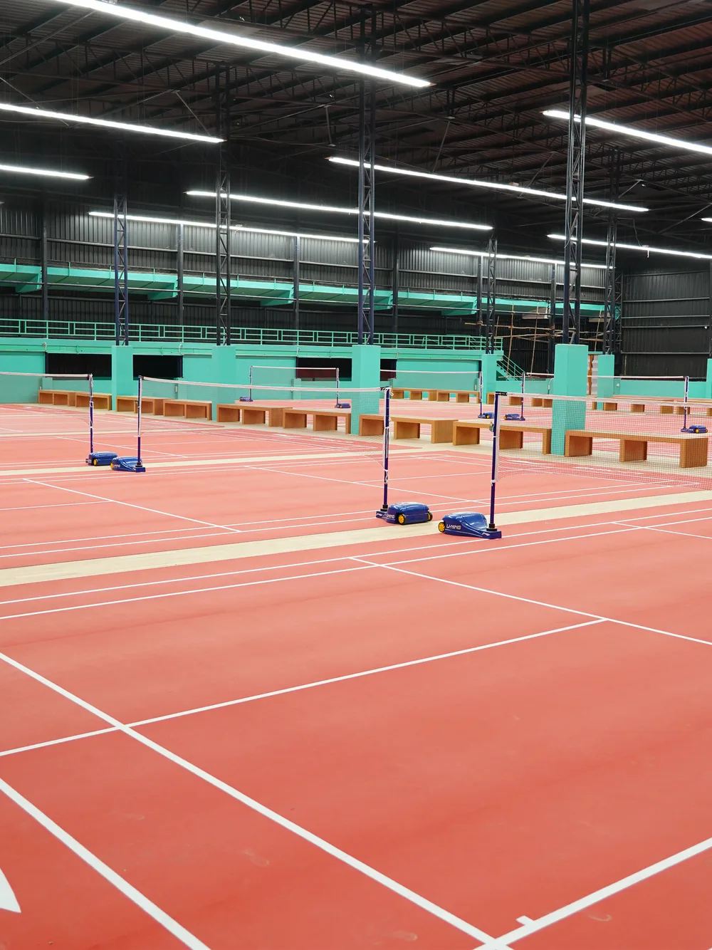 Rows of red indoor badminton courts under the hall lights