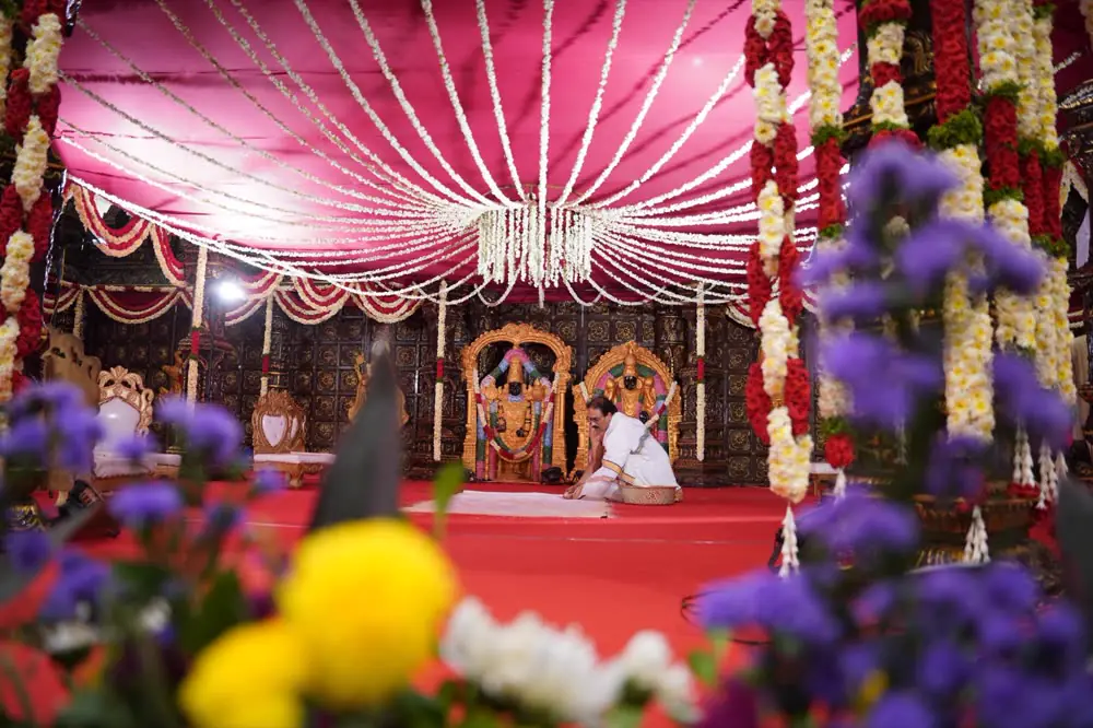 A priest at the ritual inside a garlanded mandap, seen through marigolds