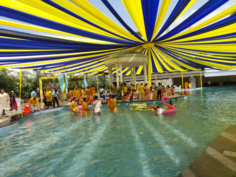 A haldi party at the pool under a blue-and-yellow canopy of ribbons
